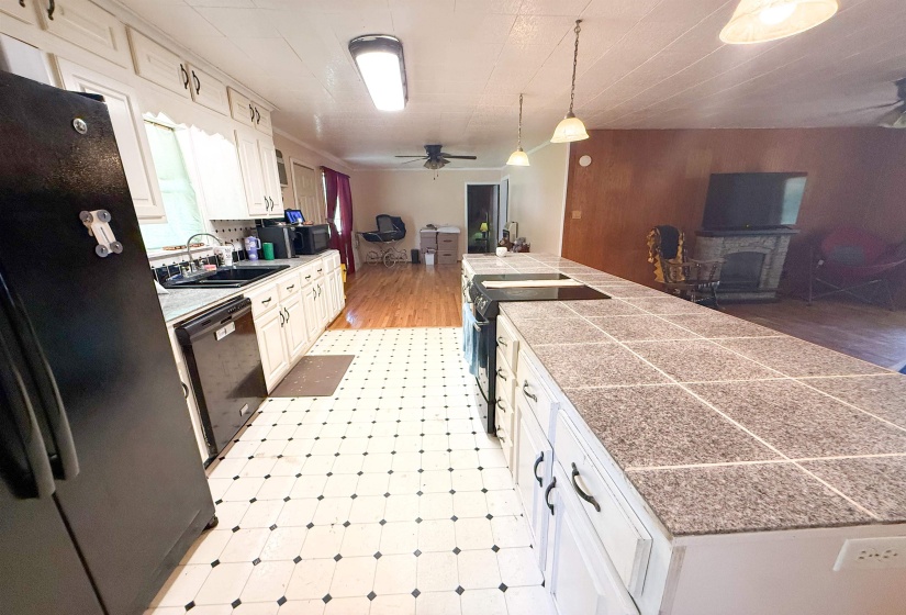 Kitchen featuring a large tile-top island with integrated cooktop, white cabinetry with black hardware, and black and white checkered flooring