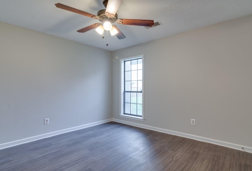 Spacious room featuring wood-finish flooring, a ceiling fan with integrated lighting, and a multi-pane window