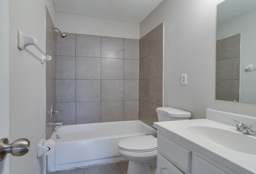 Bathroom featuring a white bathtub, gray tile surround, and a white vanity with an integrated sink and mirror