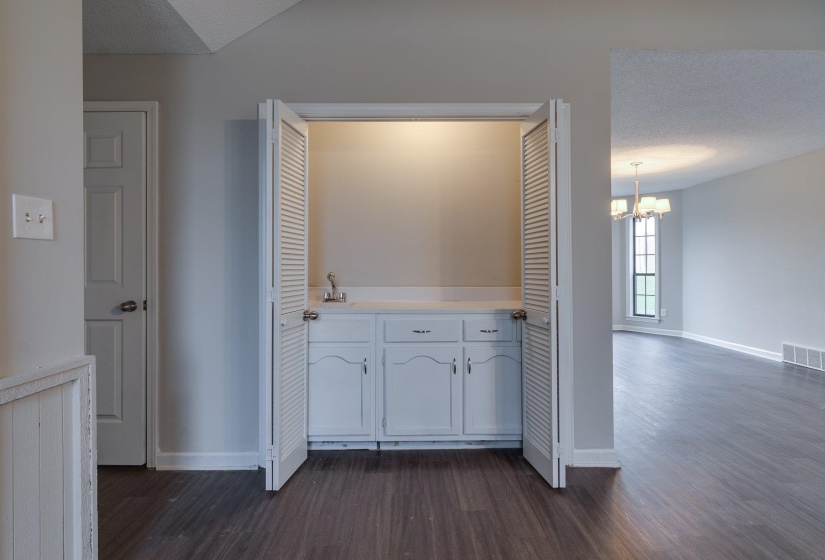 Built-in wet bar featuring a cabinet with white doors, a white countertop, a sink with a faucet, and louvered bi-fold doors