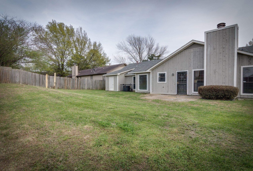 Expansive backyard featuring a wood privacy fence, detached storage shed, mature trees, concrete patio, and direct access to the interior