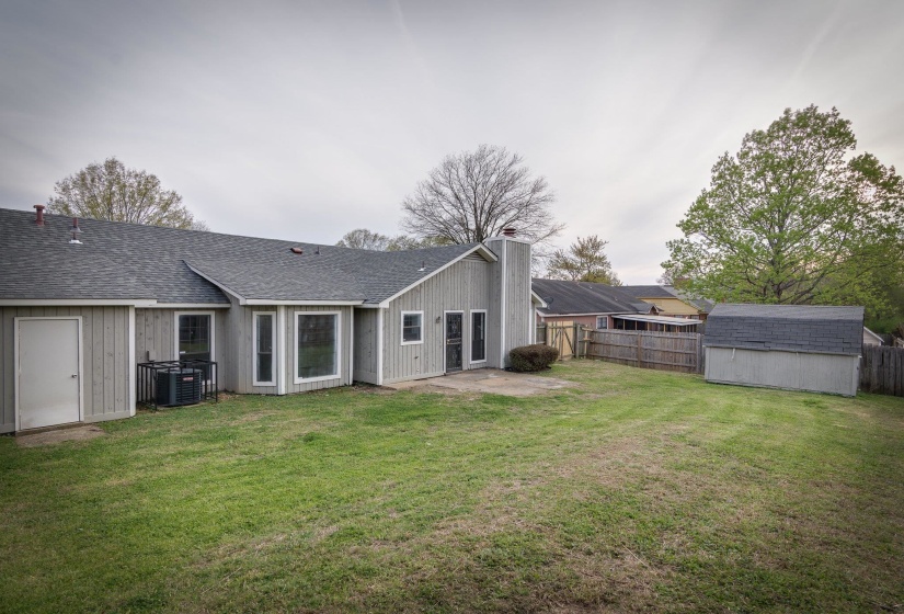 Expansive backyard featuring a manicured lawn, a detached storage shed, a privacy fence, and a concrete patio