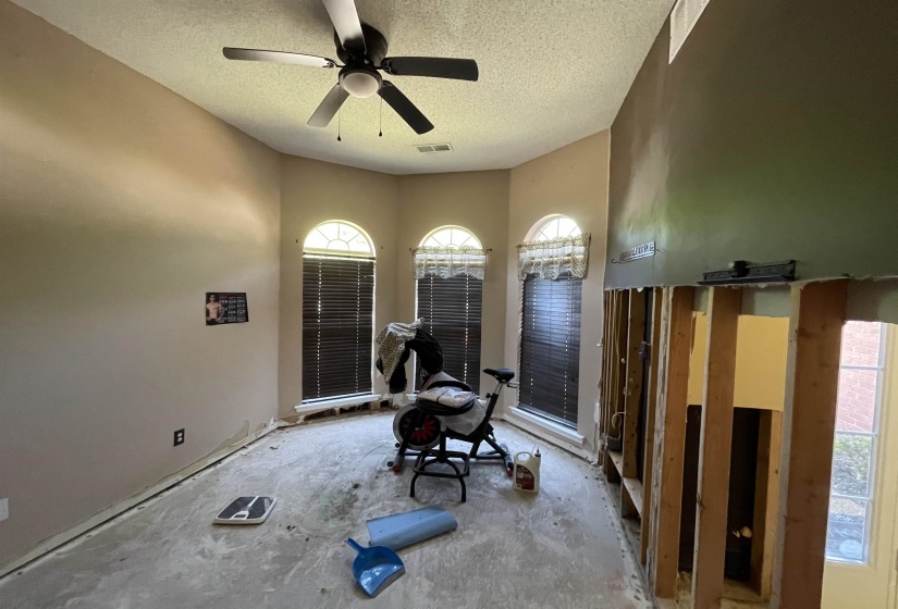 Spacious room featuring a ceiling fan, three arched windows with blinds, and exposed wall framing