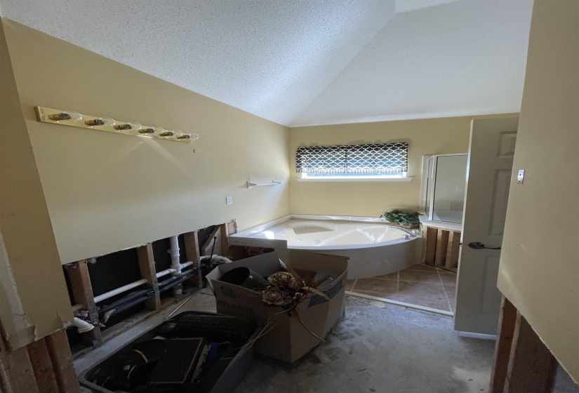 Corner soaking tub with tile surround and a window with patterned blinds