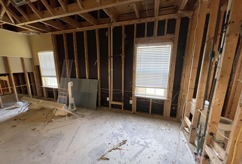 Spacious room featuring exposed wall studs and ceiling joists, two windows with blinds, and existing electrical wiring