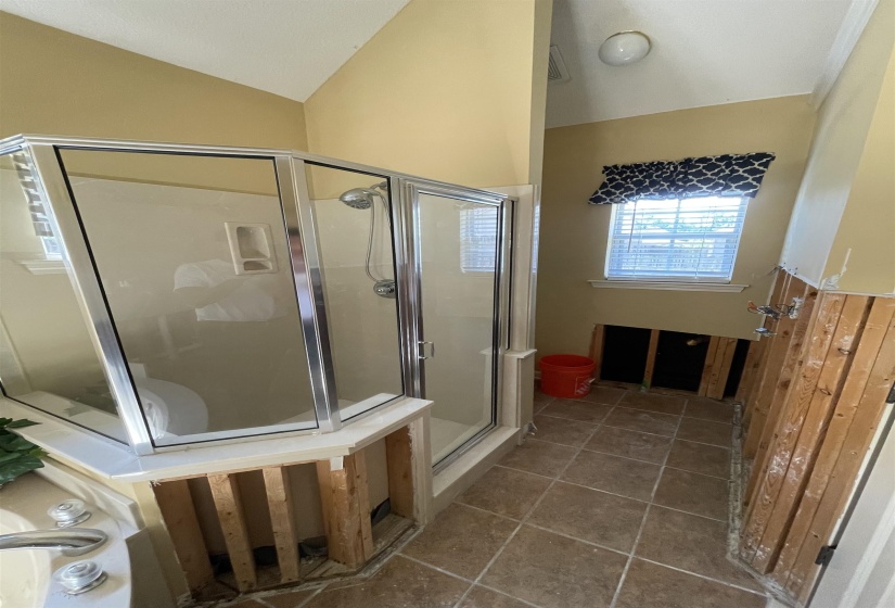 Corner shower enclosure with glass panels and chrome framing, featuring a built-in shelf