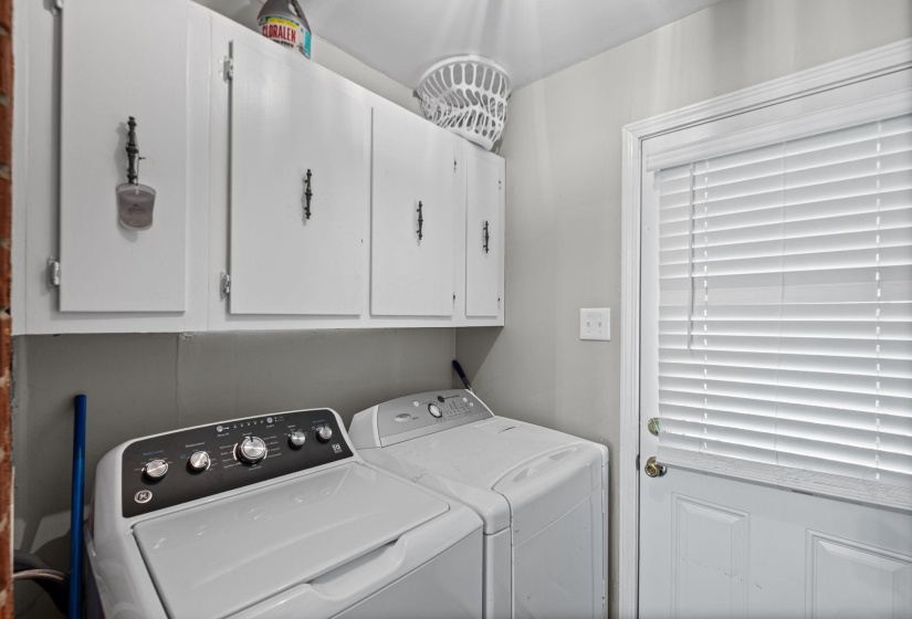 Utility area featuring white upper cabinetry with dark hardware, a paneled door with horizontal blinds, and light gray wall finishes