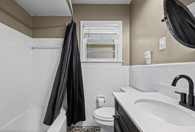Bathroom featuring a white subway tile surround, white bathtub, dark wood-finish vanity with white countertop, and matte black faucet