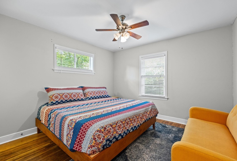 Light-filled room featuring wood-finish flooring, a ceiling fan with integrated lighting, and two windows with blinds