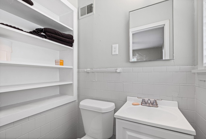 Bathroom featuring a wall-mounted mirror, built-in shelving, white subway tile wainscoting, and a white vanity with integrated sink