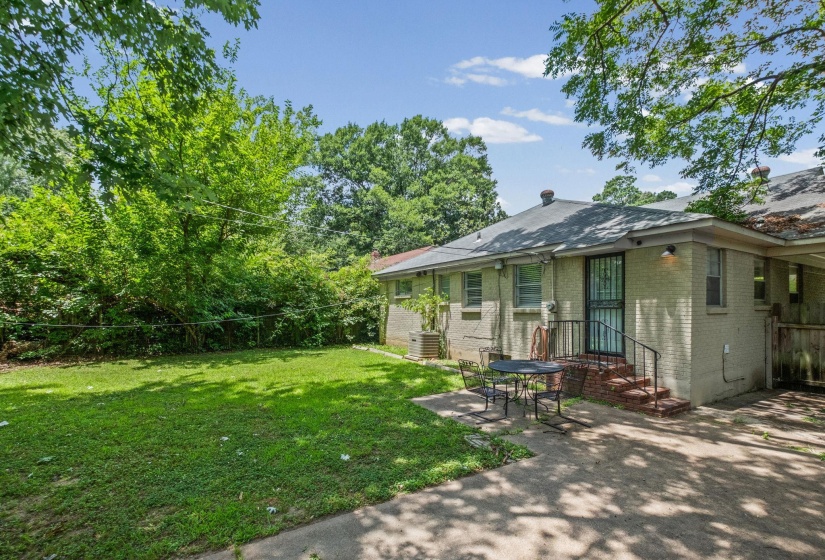 Expansive backyard featuring a manicured lawn, concrete patio, and mature perimeter foliage