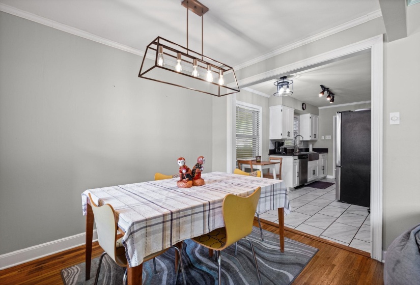 Dining area featuring warm wood-finish flooring, crown molding, and a modern linear chandelier