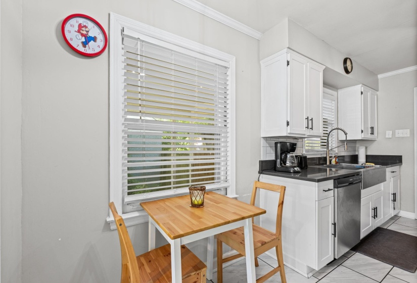 Kitchen featuring white cabinetry, dark countertops, a stainless steel dishwasher, and a farmhouse-style sink