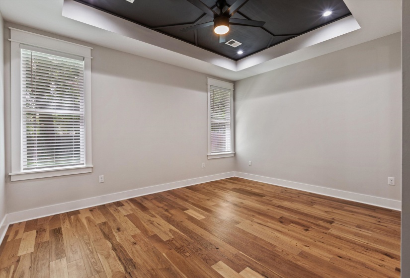 Spacious room featuring wood-finish flooring, a tray ceiling with recessed lighting and a ceiling fan, and two windows with white blinds