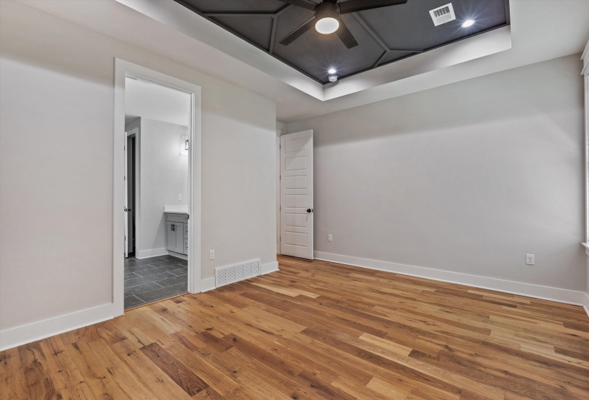 Spacious room featuring wood-finish flooring and a tray ceiling with a ceiling fan