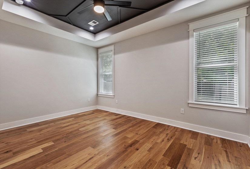 Spacious room featuring rich wood-finish flooring, a contemporary ceiling fan, recessed lighting, and a unique geometric tray ceiling design