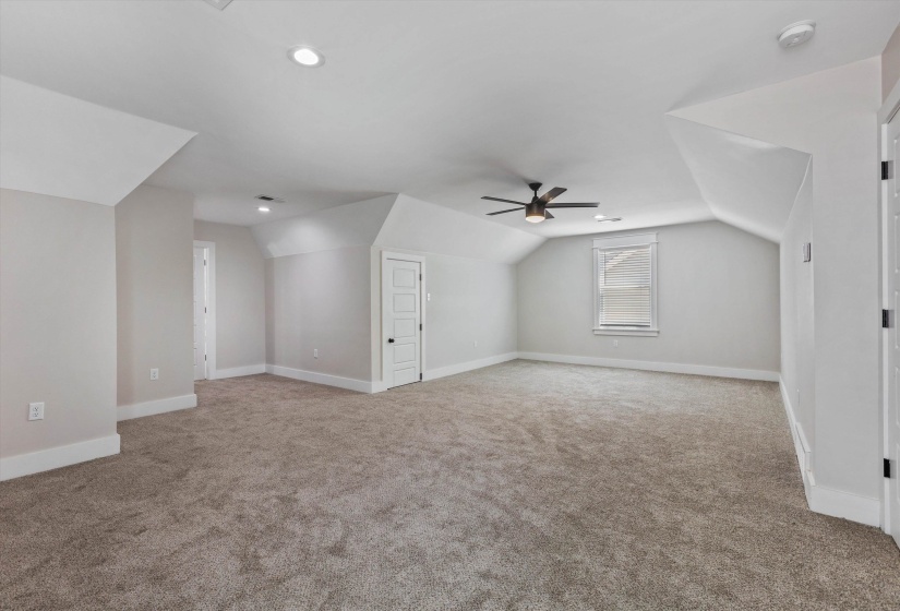 Expansive carpeted room featuring a ceiling fan, recessed lighting, and a window with blinds