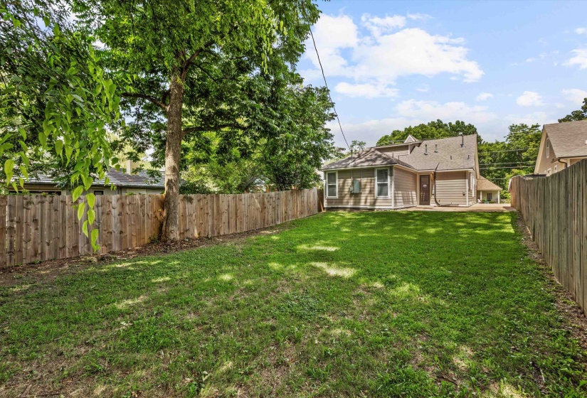 Expansive backyard featuring a lush lawn, mature trees, and a full privacy fence