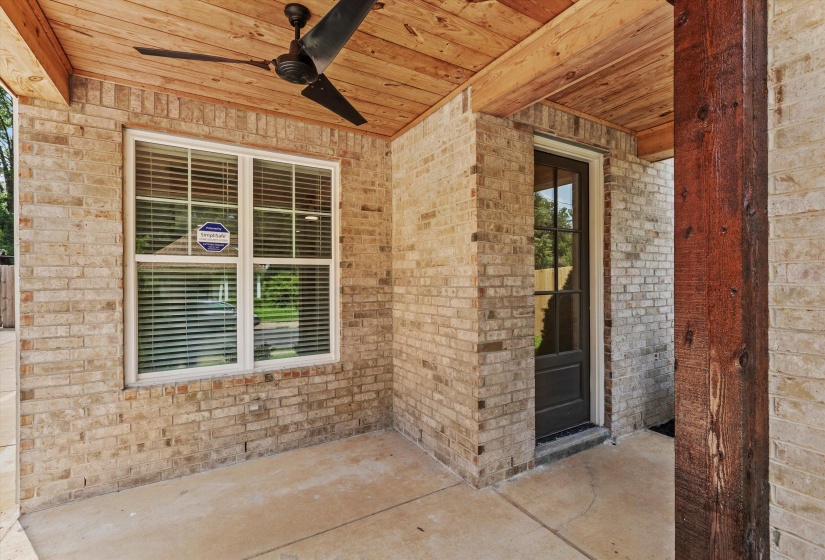 Covered patio featuring a light brick exterior, dark wood-finish ceiling, and a matching dark-blade ceiling fan