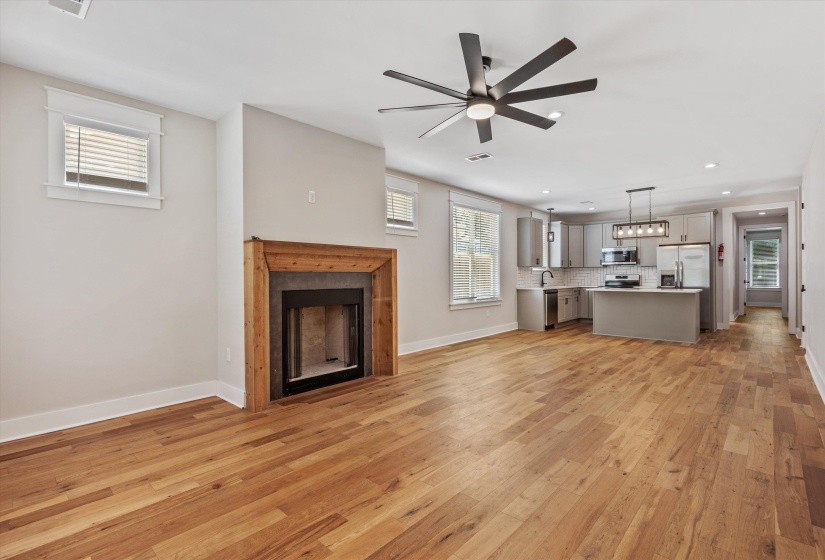 Open-concept living space featuring wood-finish flooring, a modern ceiling fan, a fireplace with a natural wood surround, a contemporary kitchen, and recessed lighting