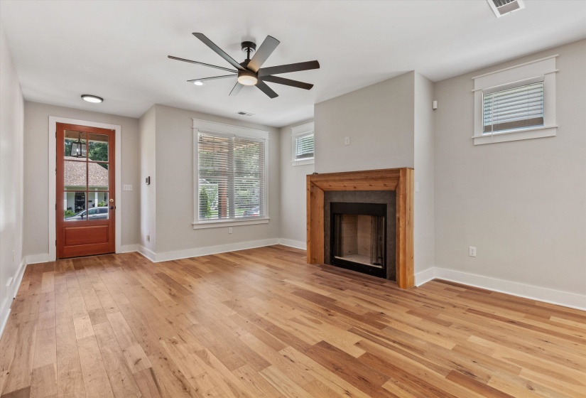 Spacious living area featuring wood-finish flooring, a modern ceiling fan, and a fireplace with a wood surround
