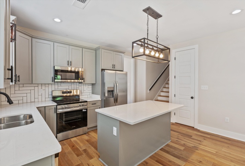 Modern kitchen featuring stainless steel appliances, light gray cabinetry, white countertops, and a herringbone tile backsplash