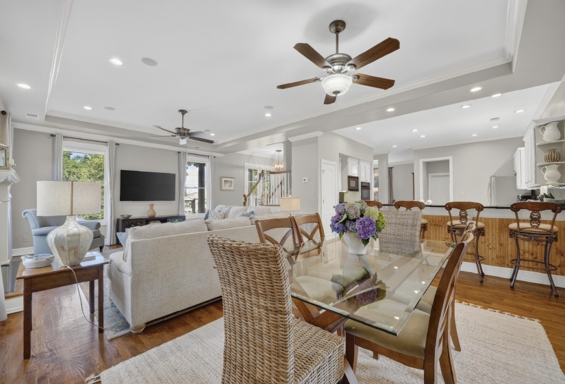 Open-concept living and dining area featuring wood-finish flooring, recessed lighting, and tray ceilings