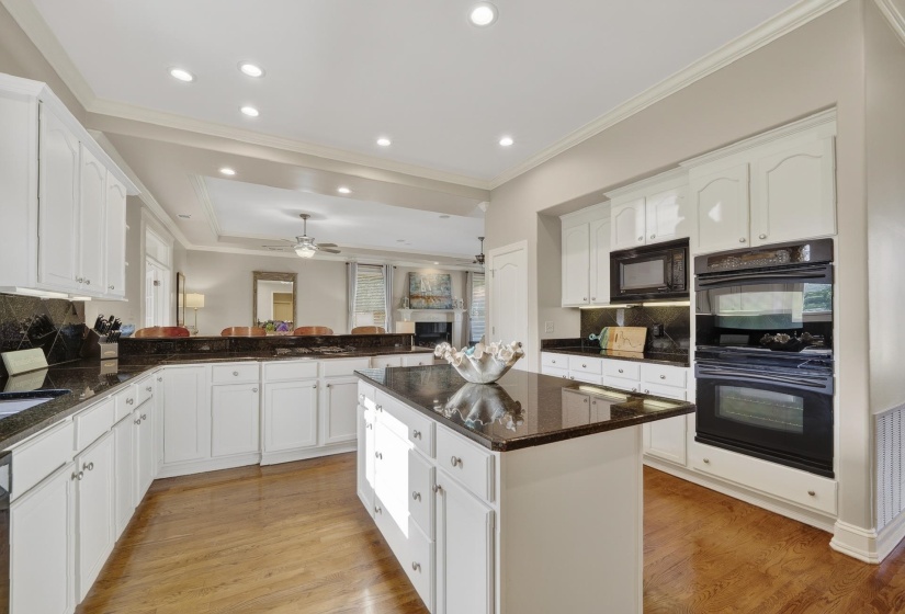 Kitchen featuring white cabinetry, dark stone countertops, wood-finish flooring, a central island, and built-in double ovens
