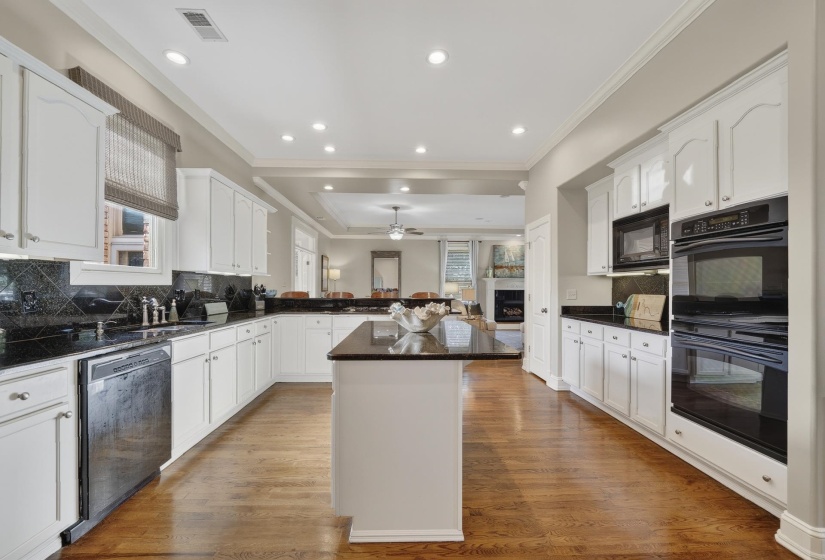 Bright kitchen featuring white cabinetry, black countertops, wood-finish flooring, a stainless steel dishwasher, and built-in double ovens