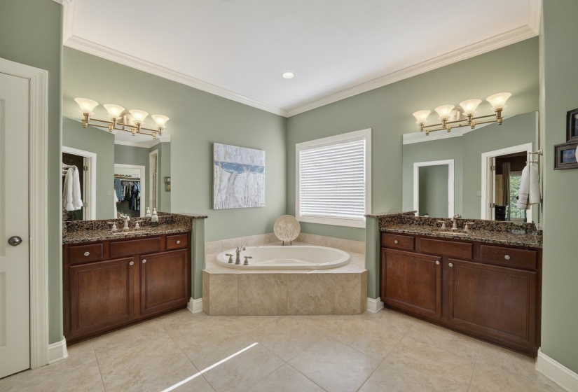 Bathroom featuring a corner soaking tub, dual vanities with granite countertops, and tile flooring