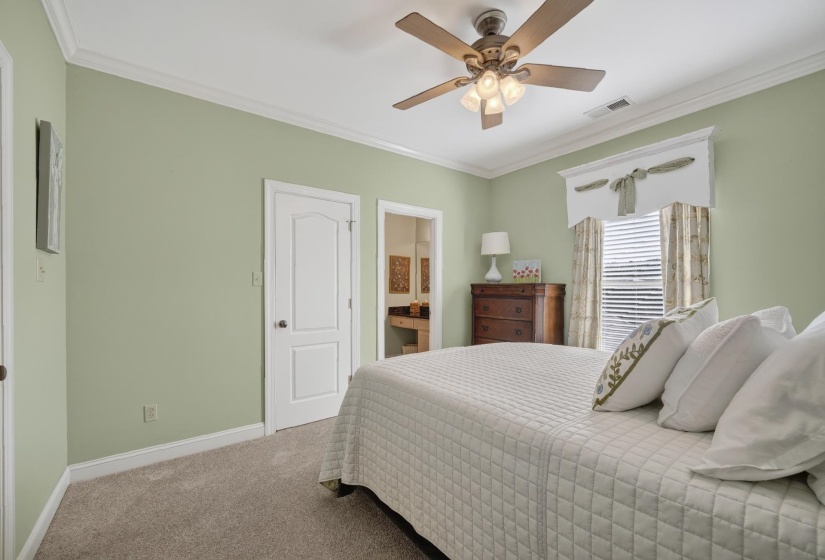 Spacious bedroom featuring light green walls, crown molding, and neutral carpet flooring