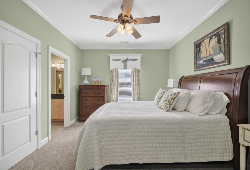 Carpeted bedroom featuring a ceiling fan with integrated lighting, crown molding, and a paneled white door