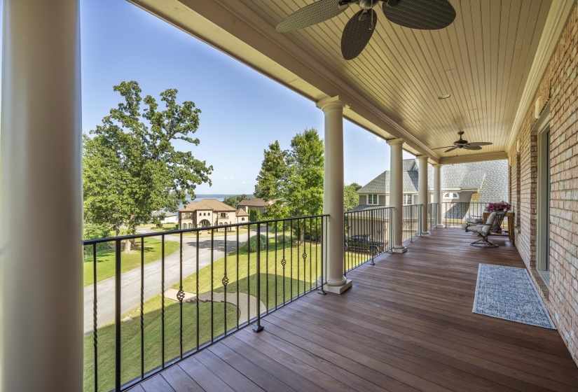 Expansive covered balcony featuring wood-finish flooring, brick exterior, ceiling fans, decorative pillars, and black wrought iron railing