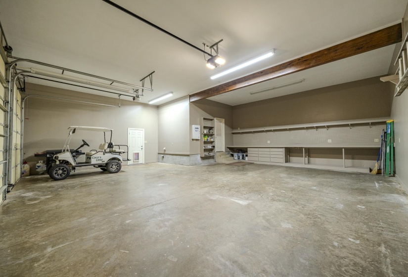 Spacious garage featuring a concrete floor, exposed wood beam, extensive built-in shelving, integrated cabinetry, and multiple fluorescent light fixtures