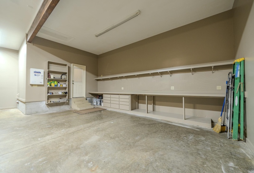 Concrete flooring garage featuring a built-in workbench, integrated shelving, additional wall shelving, and a full-light door