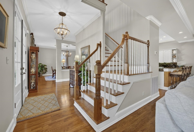 Hardwood flooring throughout the entry, staircase with wood handrails and white balusters, and crown molding accents