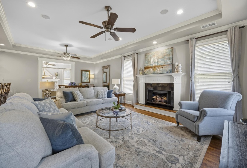 Spacious living area featuring a fireplace with a white mantel, wood-finish flooring, recessed lighting, and tray ceilings
