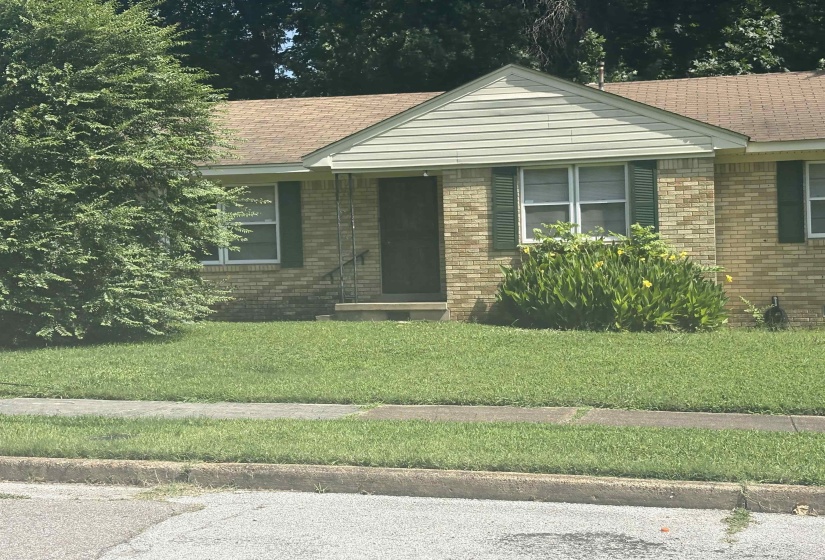 Brick exterior featuring green shutters, white window frames, and a brown shingled roof
