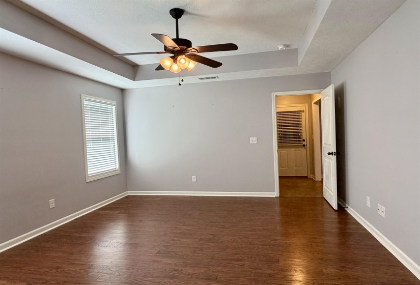 Spacious room featuring tray ceilings, a ceiling fan with integrated lighting, wood-finish flooring, and crisp white trim