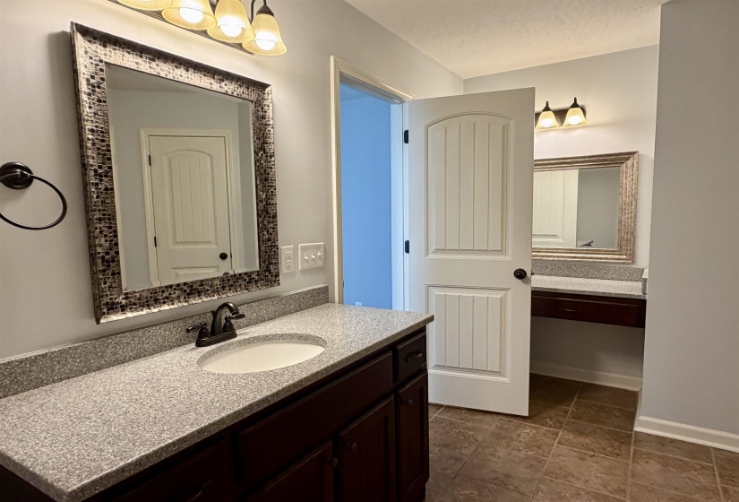 Bathroom vanity featuring a speckled countertop, integrated sink, dark wood-finish cabinetry, and a framed mirror with overhead lighting
