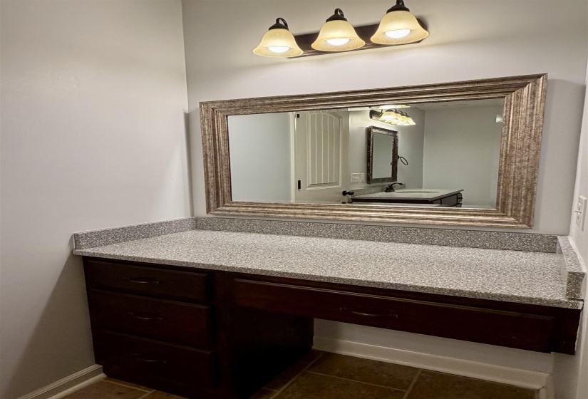 Built-in vanity featuring a speckled countertop, dark wood-finish cabinetry with drawer storage, and an ornate framed mirror