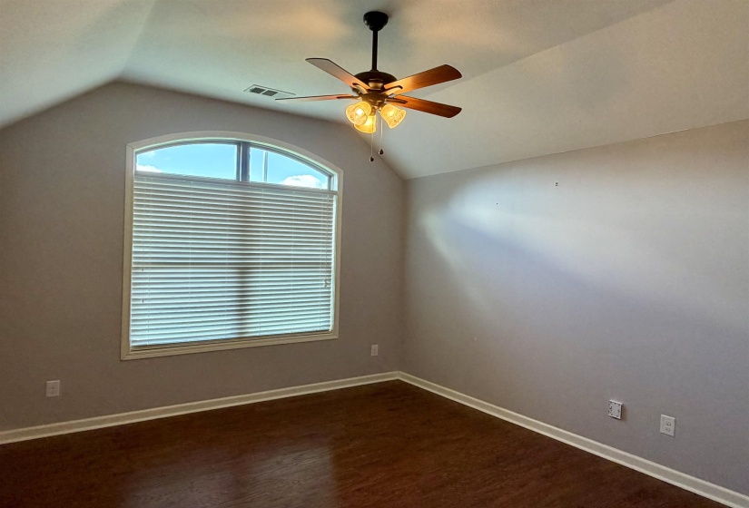 Vaulted ceiling room featuring an arched window with blinds, a ceiling fan with integrated lighting, wood-finish flooring, and light gray walls