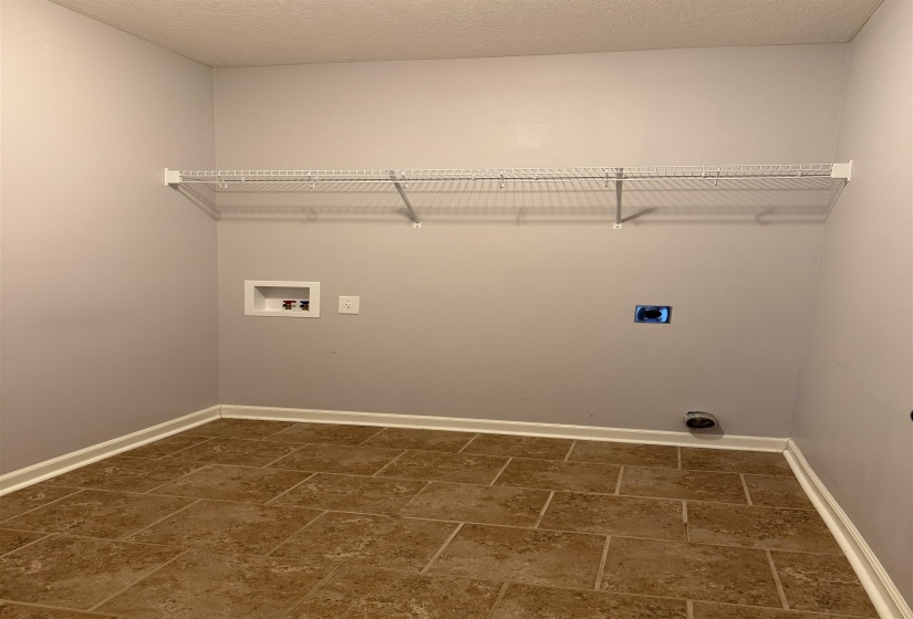 Laundry area featuring tile flooring, neutral wall paint, white baseboards, and an overhead wire shelving unit