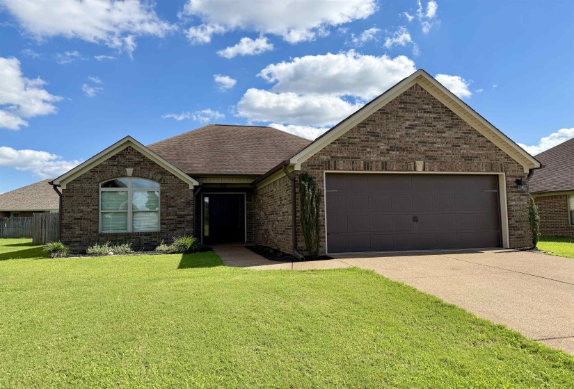 Brick facade residence featuring an attached two-car garage, arched window, covered entryway, and established front landscaping
