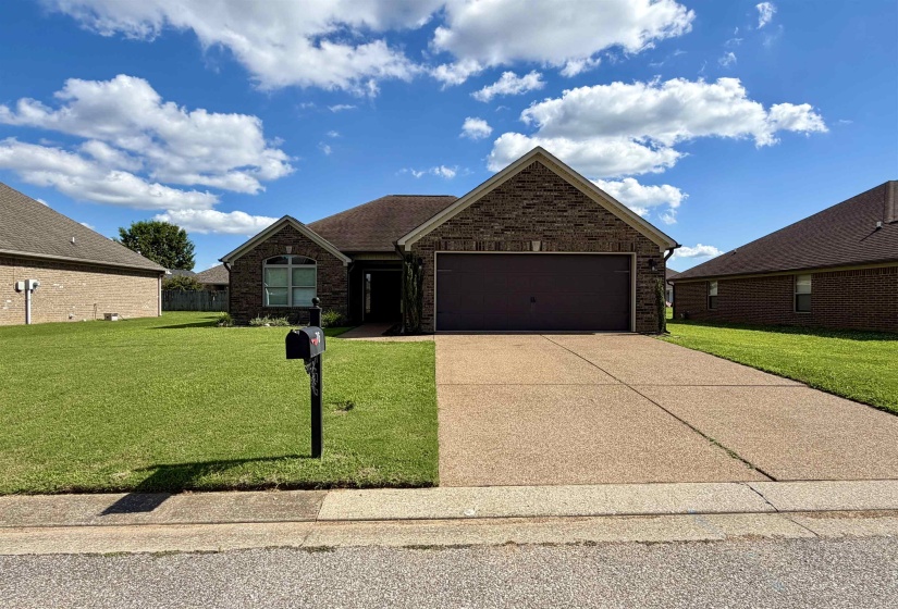 Brick-front residence featuring a two-car garage, a concrete driveway, and a manicured lawn