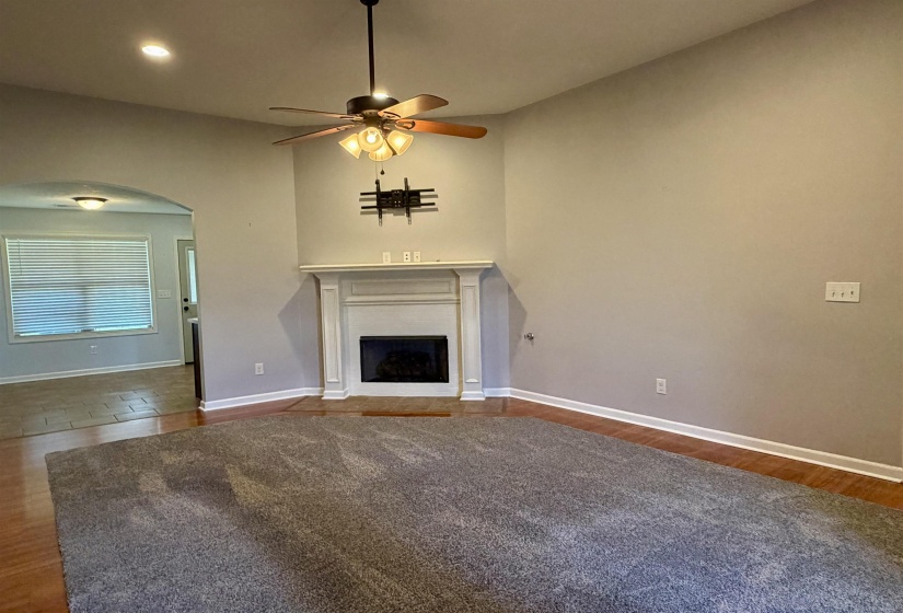 Living area featuring a white mantel fireplace, wood-finish flooring, and a ceiling fan with integrated lighting
