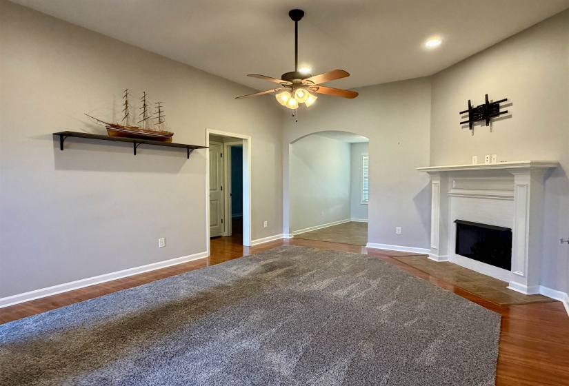 Living area featuring a fireplace with a white mantel, wood-finish flooring, and a ceiling fan