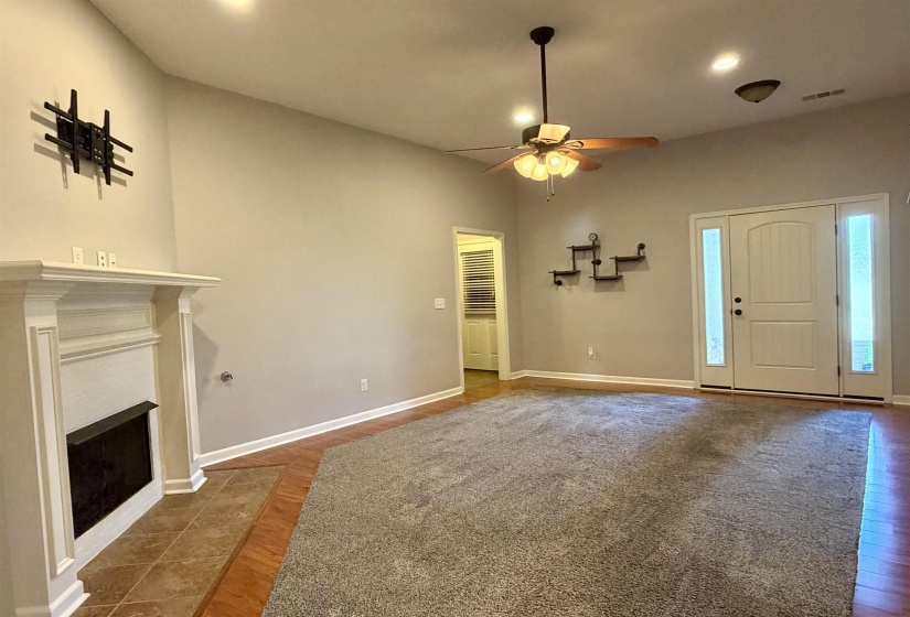 Spacious living area featuring a fireplace with white mantel, a ceiling fan with integrated lighting, recessed lighting, and a front entry door with sidelight windows