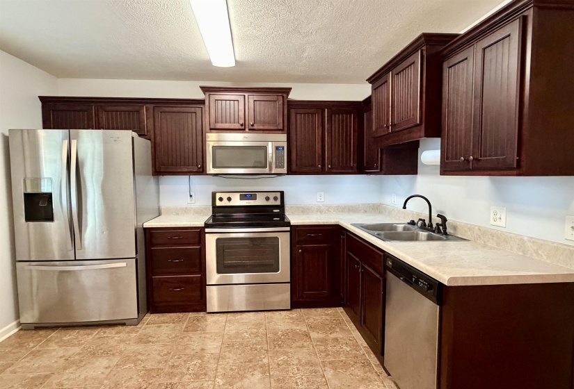 Kitchen featuring dark wood cabinetry, light-toned countertops, and stainless steel appliances including a refrigerator, range, microwave, and dishwasher