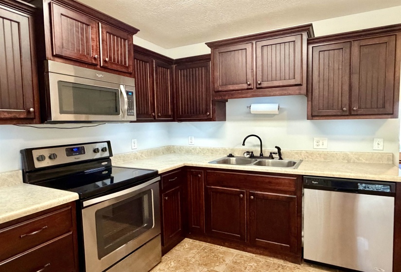 Kitchen featuring dark wood-finish cabinetry, light-toned countertops, and a full suite of stainless steel appliances